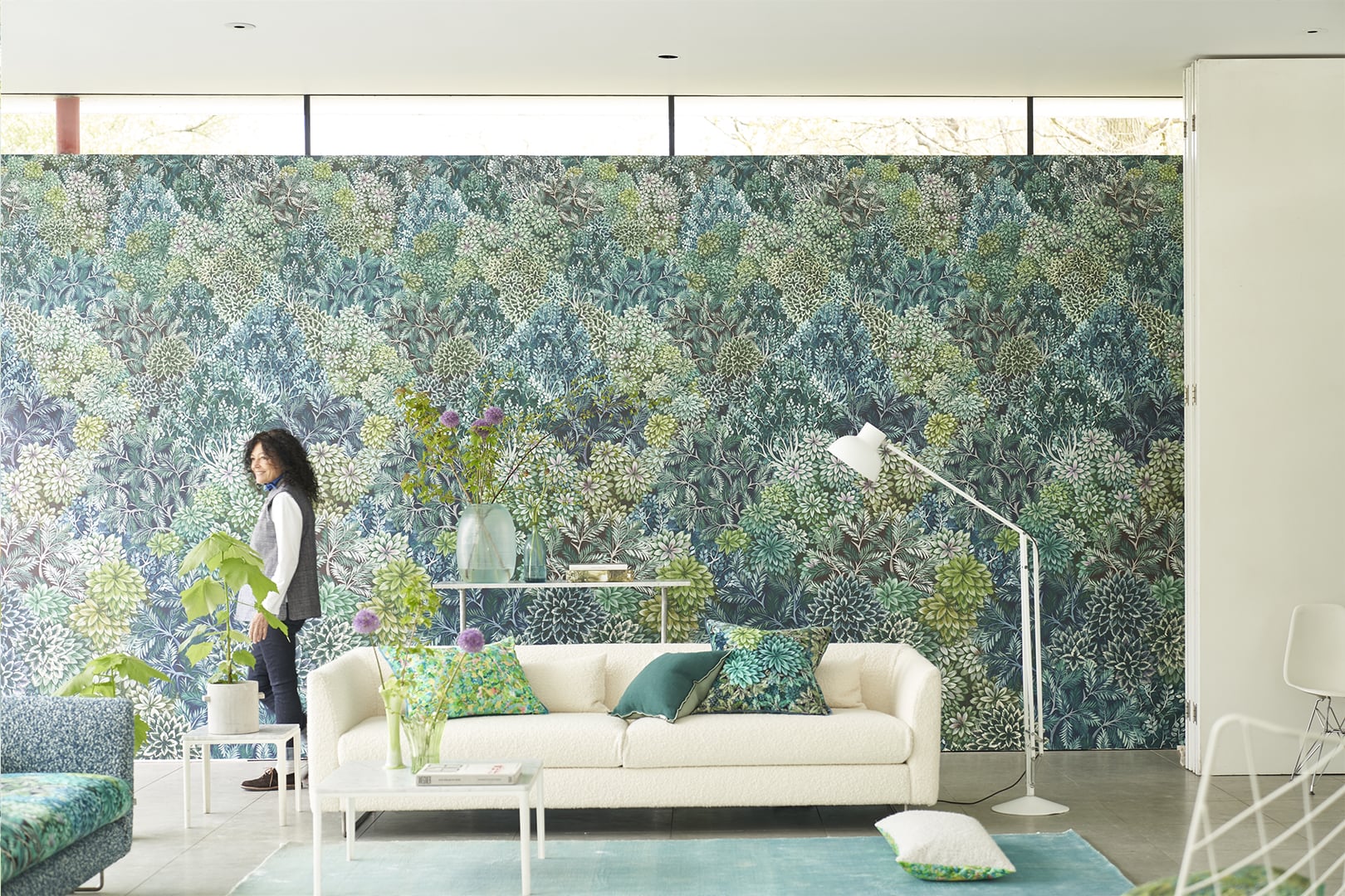 Sunlit room with blue and green botanical wallpaper behind a pale sofa