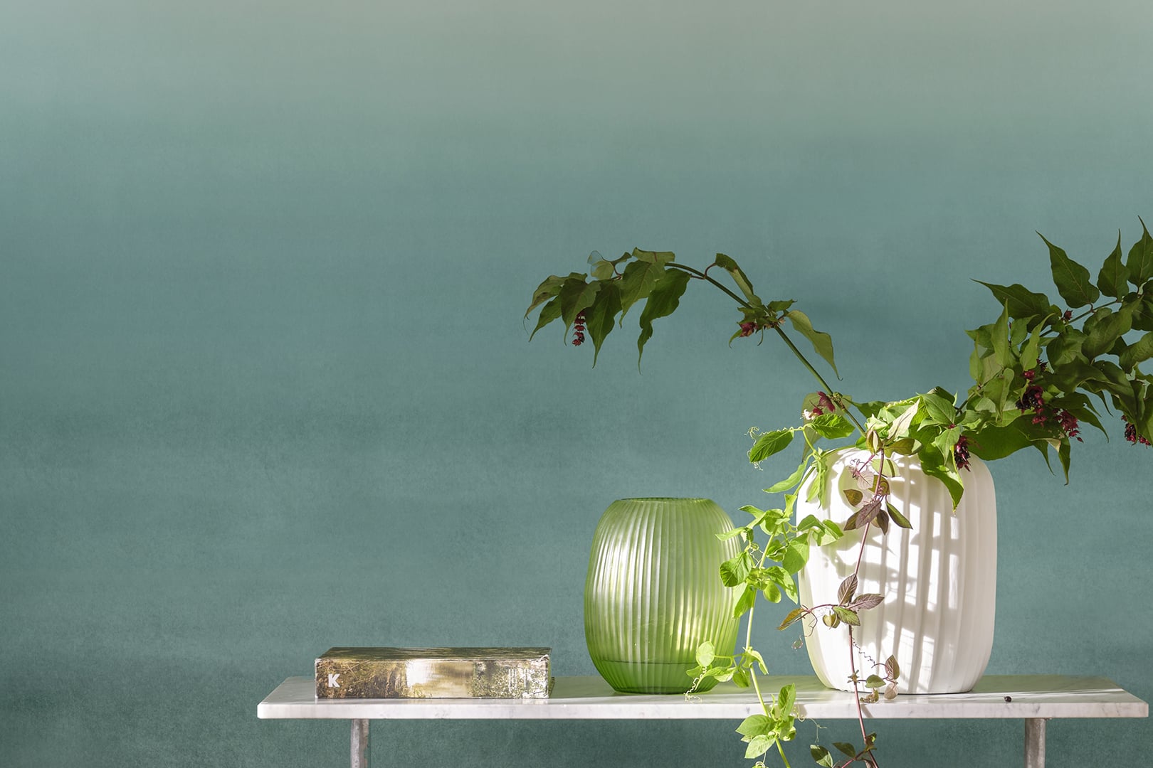 Close-up of ombré green wallpaper with glass vase and sculptural branch